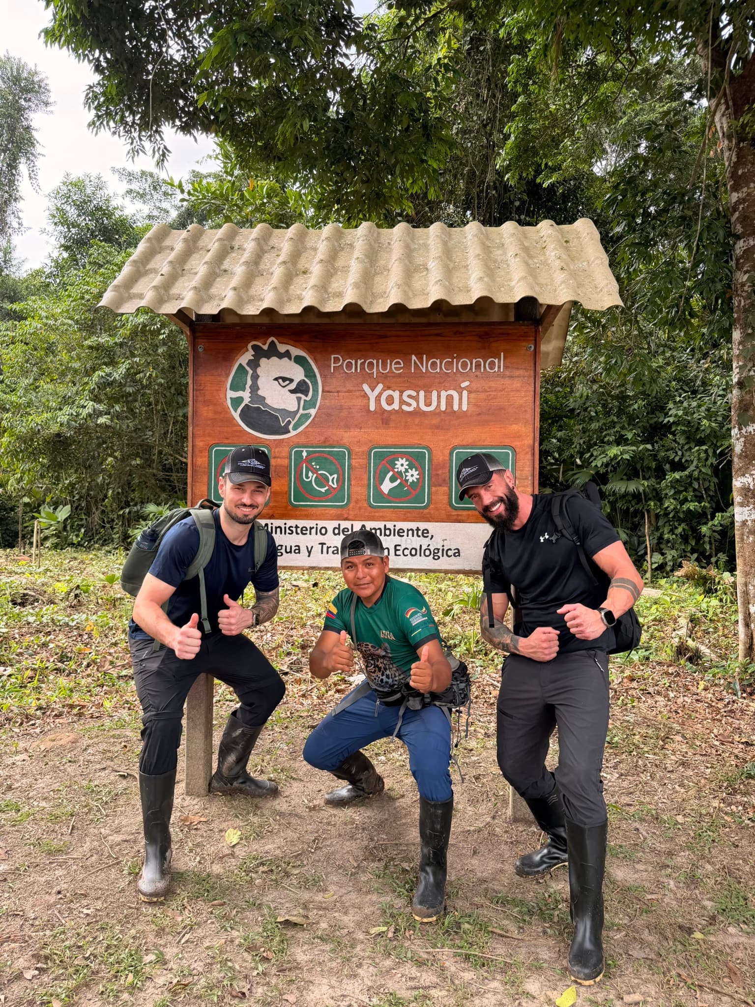 Tres hombres con botas de caucho posan frente al letrero del Parque Nacional Yasuní en Ecuador.